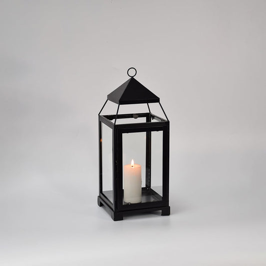 Black metal glass lantern with candle lit shown on white background highlighting warm glow classic frame design and home decor use.