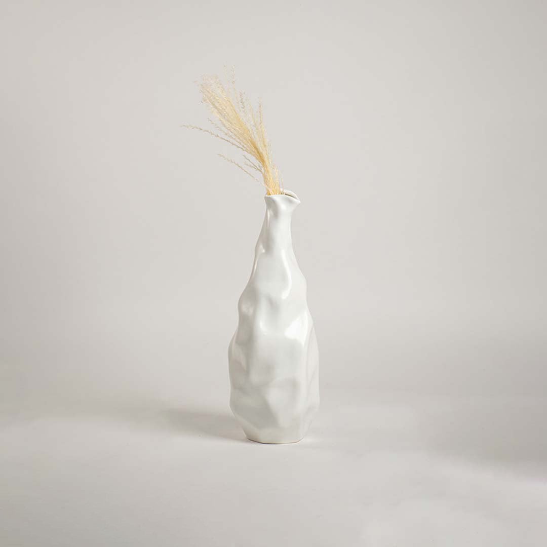 A modern sculpted white ceramic vase placed on a soft white backdrop focusing on its tall organic silhouette and elegant handcrafted style.