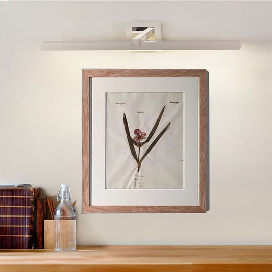 Closeup lifestyle view of silver metal picture light on a styled interior wall adding warm accent lighting.