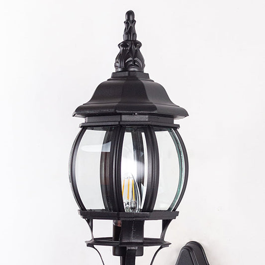 Closeup of black upward wall lantern showing curved glass cage scroll bracket detail and decorative finial vintage design.
