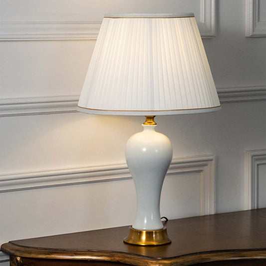 White ceramic table lamp with pleated fabric shade and brass base adding timeless traditional ambient lighting indoors.