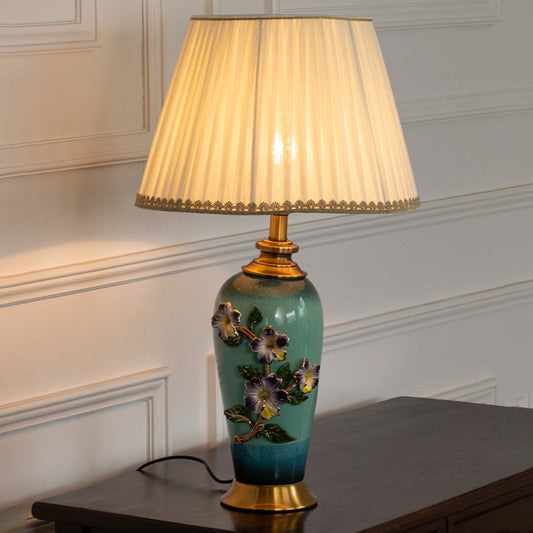 Green floral ceramic table lamp with pleated fabric shade offering elegant classic decor and ambient lighting indoors.