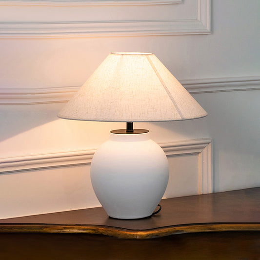 White ceramic table lamp with fabric shade displayed on a wooden console table creating warm ambient lighting indoors.