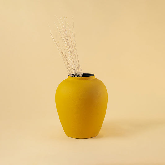 Minimalist matte yellow rounded metal vase with twigs for cozy home decor and artistic shelf display needs.