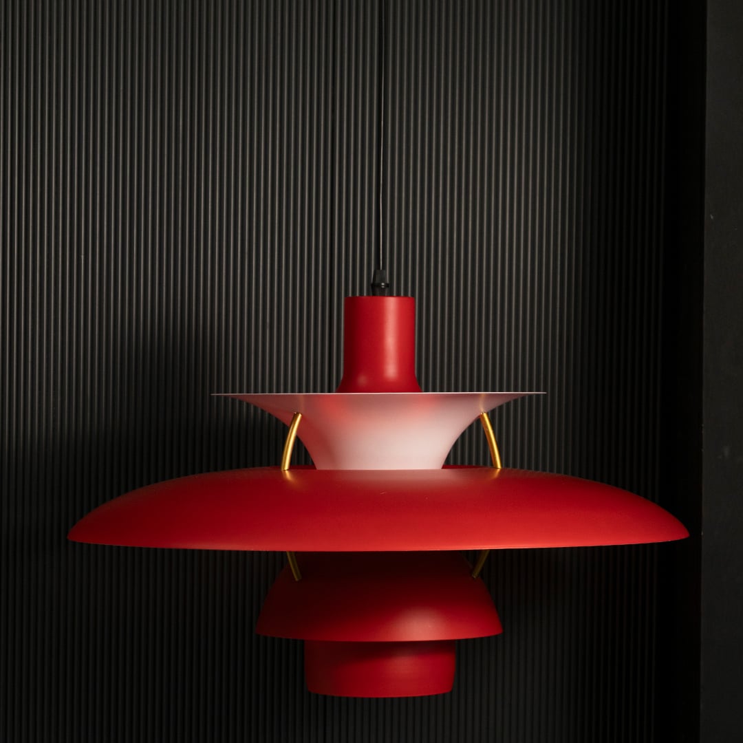 Red metal pendant light switched on against black background creating warm focused illumination for modern dining interiors.