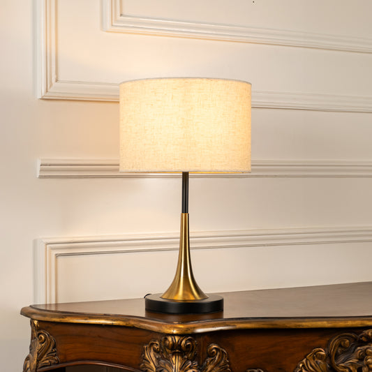 Brass metal table lamp with fabric drum shade displayed on a carved wooden console table creating elegant ambient lighting.