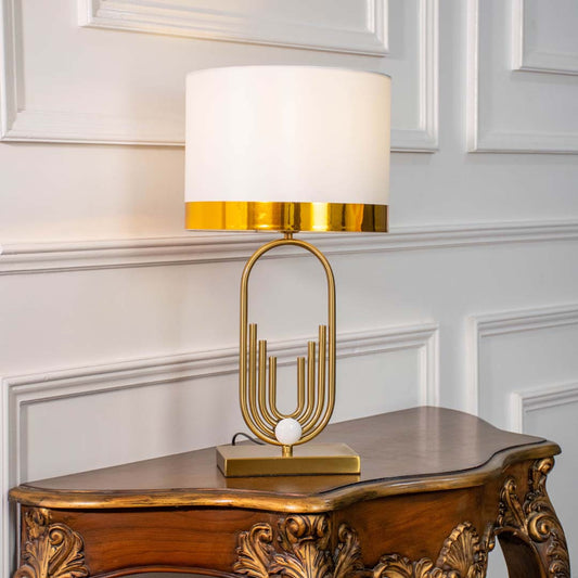 White shade gold sculptural table lamp on carved console table with light on and white panel wall background for modern luxury décor.