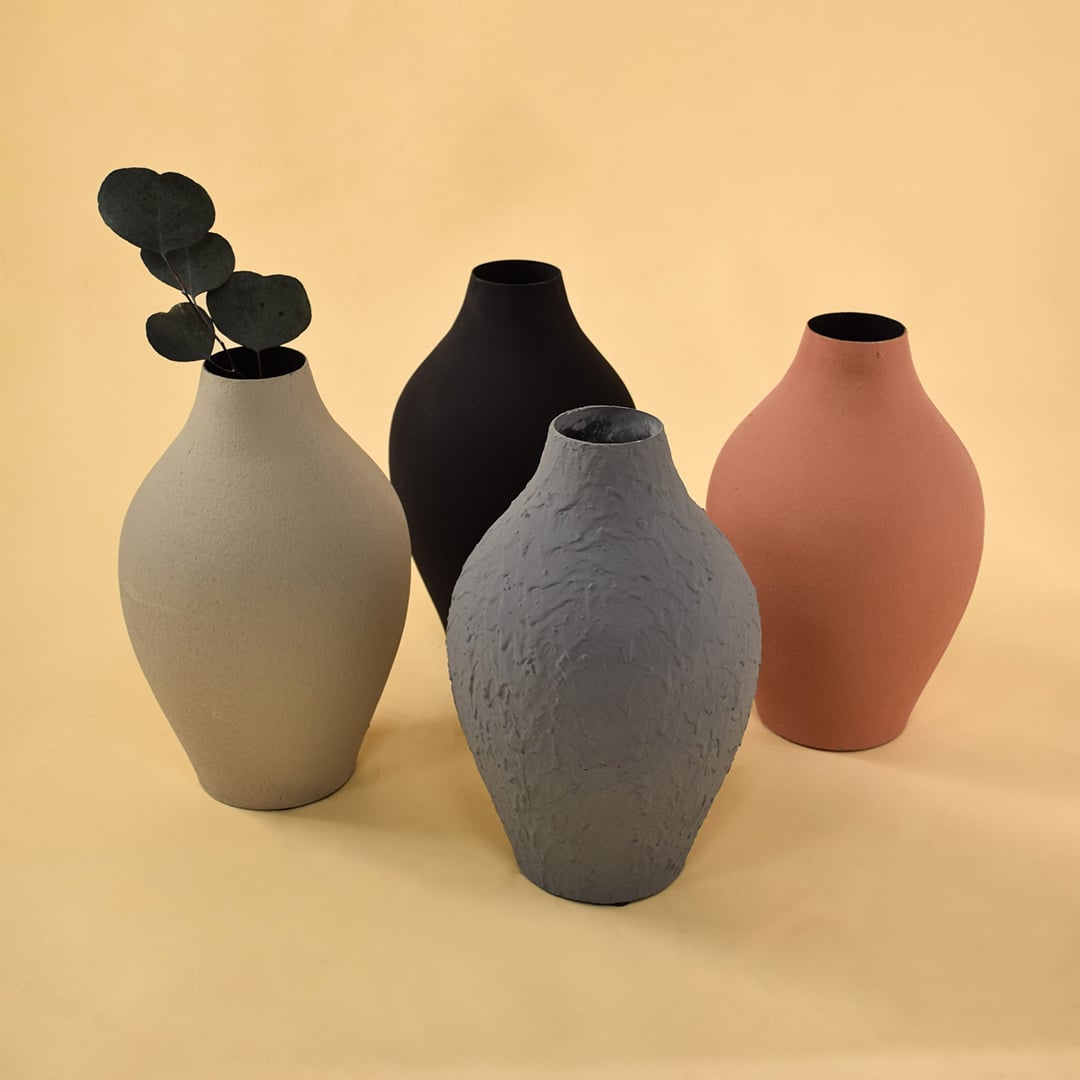 A curated arrangement of four vases in black grey terracotta and cream tones displaying varied textures and shapes for a stylish modern decor composition.