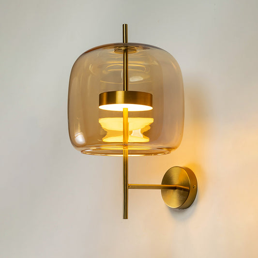 Modern wall light with gold mount and transparent glass shade on neutral background warm ambient lighting for bedroom decor.