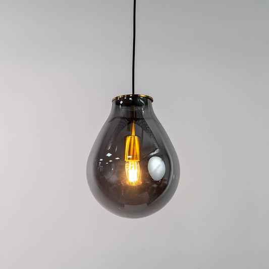 A smoked grey glass pendant light with lights on against a clean white background showing its teardrop shaped glass shade and warm glowing filament.