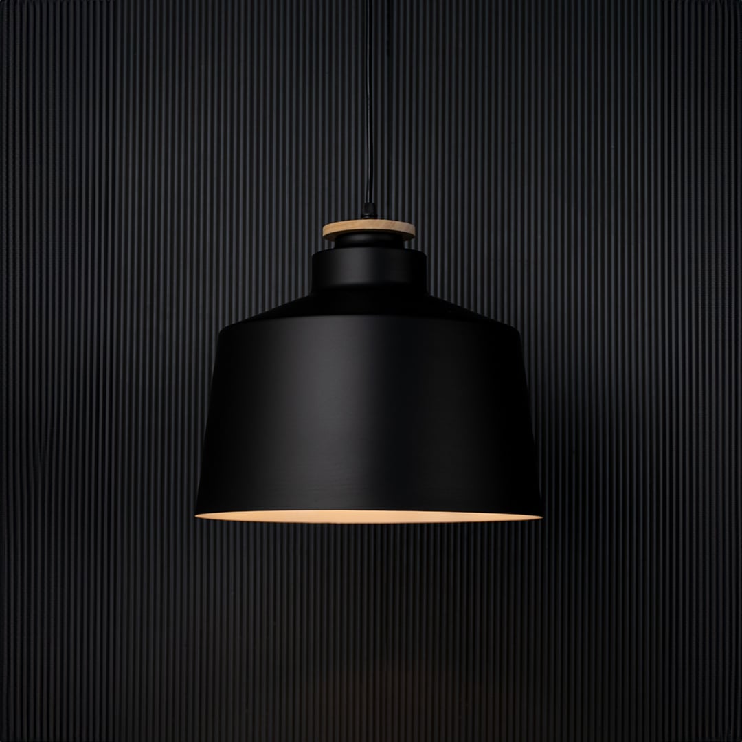 A modern black pendant lamp shown on a black background with the light on creating a soft warm glow that highlights the shape and contrasts against the dark surface.