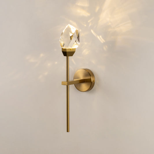 Elegant clear glass wall sconce with gold metal mount casting soft patterned light on white wall background ideal for ambient lighting setup.