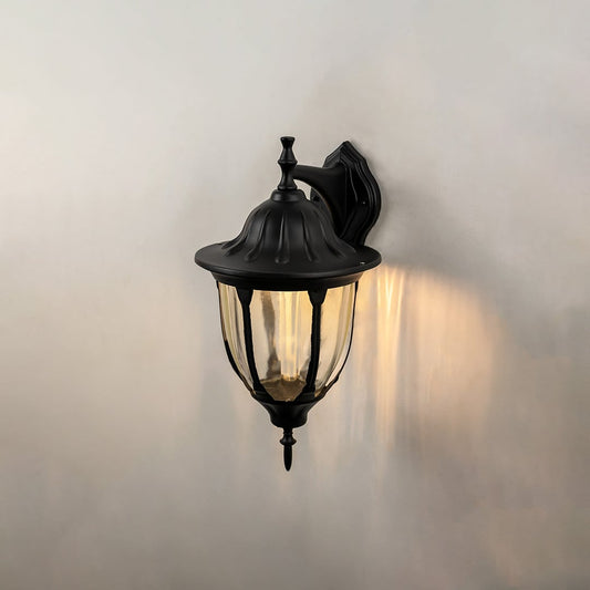 Black downward outdoor wall lantern glowing on black background highlighting traditional coach style exterior lighting warm glow.