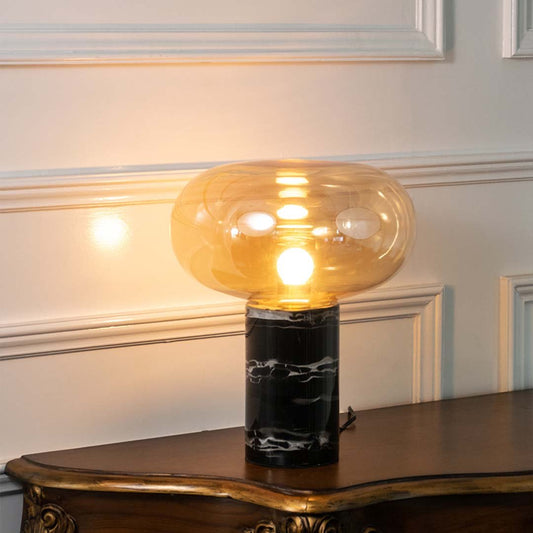 Amber smoked glass table lamp with black marble base and exposed bulb creating elegant contemporary decorative lighting.