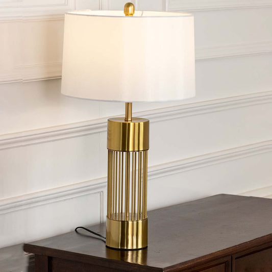 Gold metal table lamp with white fabric shade and open frame base creating elegant modern ambient lighting indoors.