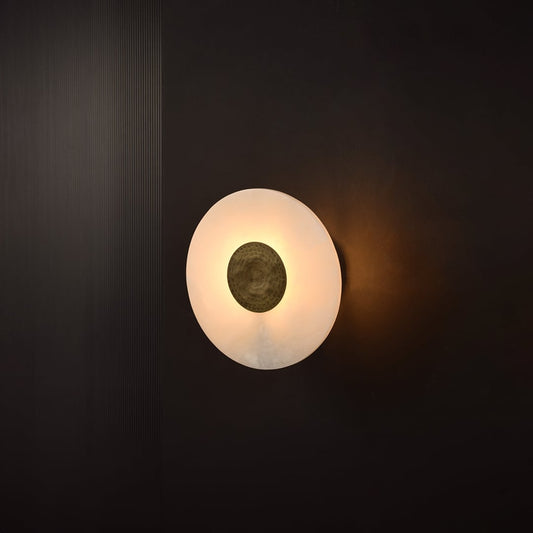 Circular marble wall light glowing on dark background highlighting gold center detail and elegant marble texture for luxury interiors.