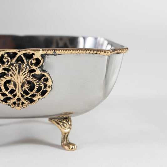 Square silver bowl with gold detailing shown partially packed in black premium gift box with lid slightly open.