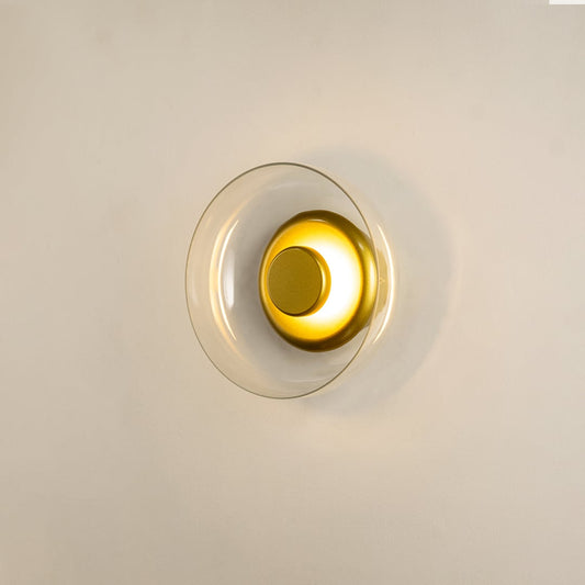 Gold wall light with clear glass shade glowing softly on white background perfect for bedrooms and hallways.