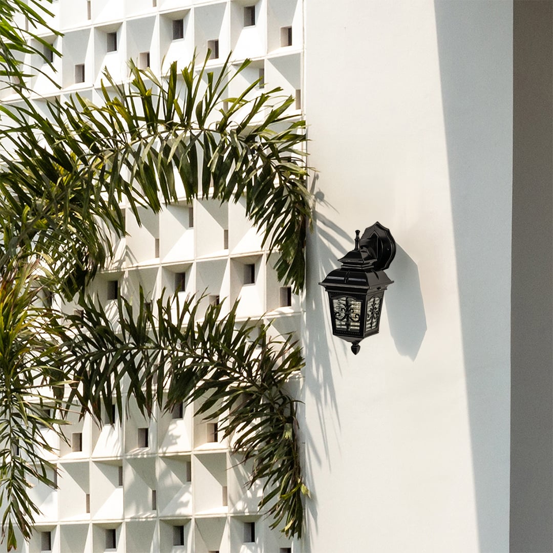 Black metal outdoor lantern mounted on a bright exterior wall with the light off showcasing its classic decorative glass panels and elegant outdoor design.