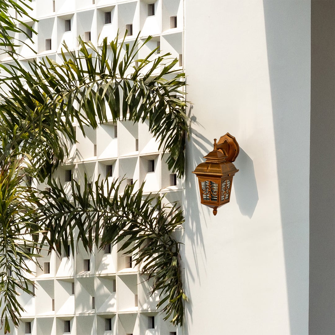Gold metal outdoor lantern mounted on a bright exterior wall with the light off showcasing its classic decorative glass and vintage outdoor wall lighting design.