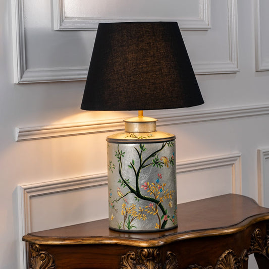 Table lamp on white background displaying ceramic base with hand painted botanical design accented by a classic black lampshade.