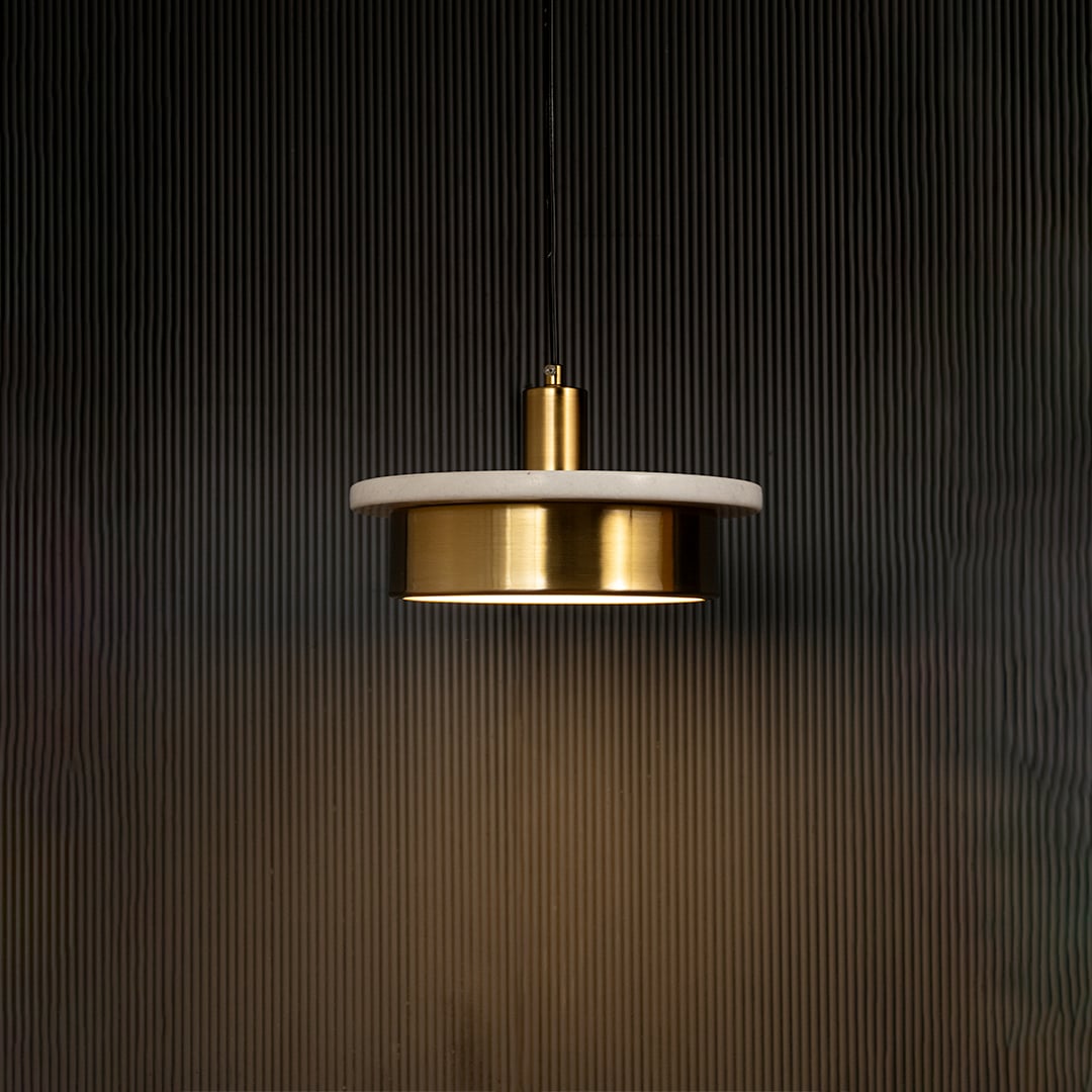 White marble and metal disc pendant light hanging against dark textured wall with light on for elegant soft décor.