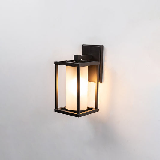 Modern black metal outdoor wall sconce with frosted glass shade illuminating a warm glow for exterior patio entry placement.