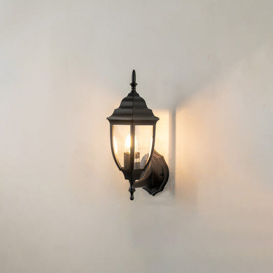 Black metal outdoor lantern wall light on white background with warm glow for classic patio decor.