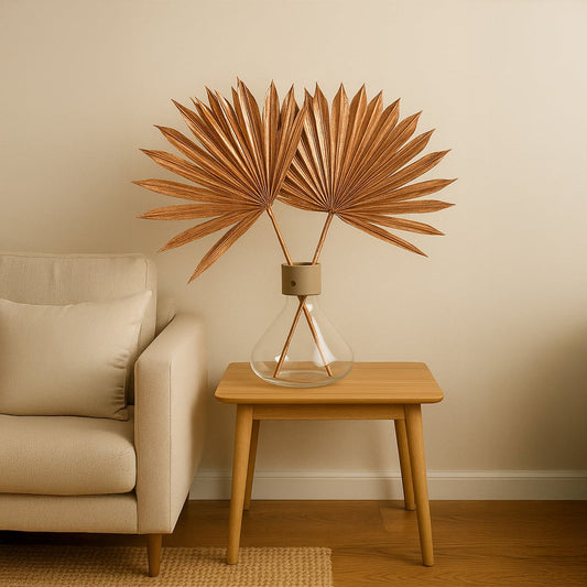 Copper dried palm leaves in a glass vase on a wooden table beside a beige sofa adding a warm modern touch to living decor.