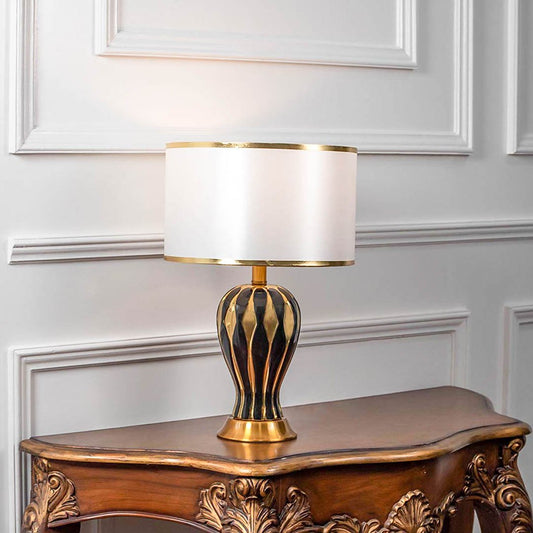 Decorative table lamp with gold metal cage base and white fabric shade on wooden table elegant lighting for bedroom decor.