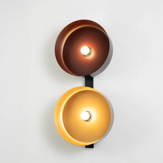 Decorative wall light in black and gold metal finish with dual disc design for bedroom or living decor lighting white background.