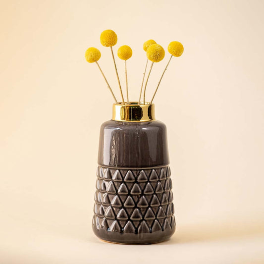 A stylish ceramic vase with a golden top holding yellow floral stems placed in a neutral toned interior setup adding a warm decorative touch to the room atmosphere.