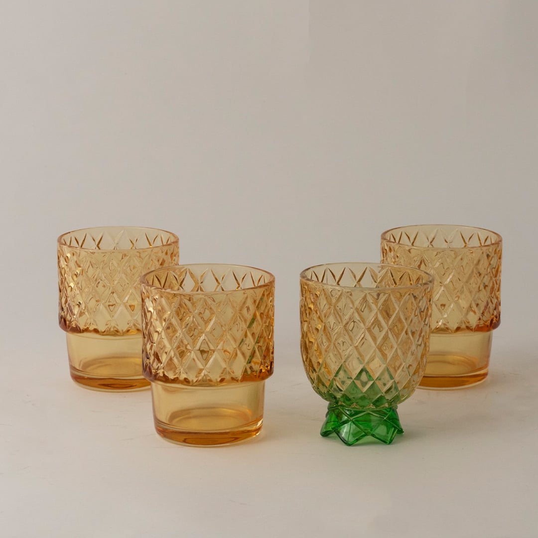 Amber pineapple shape glass tumblers with diamond pattern and green lid creating elegant look for parties and dining.