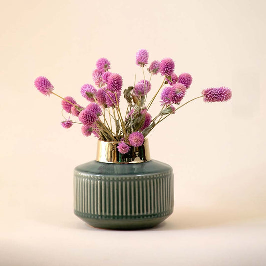Round green ceramic vase with a golden rim filled with purple globe amaranth flowers placed against a soft beige background for a charming home decor look.