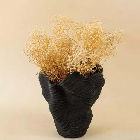 Fluffy cream yellow dried flower stems bundle arranged inside an elegant modern textured black ceramic vase on living table.
