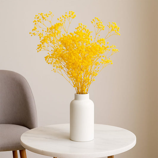 Bright yellow dried gypsophila flowers styled in white ceramic vase on round marble table modern lifestyle decor.
