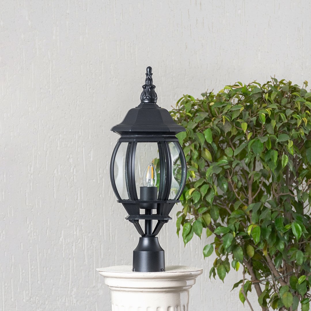 Classic black outdoor pillar lamp with clear curved glass shade placed on stone pillar ideal for entrance and garden.