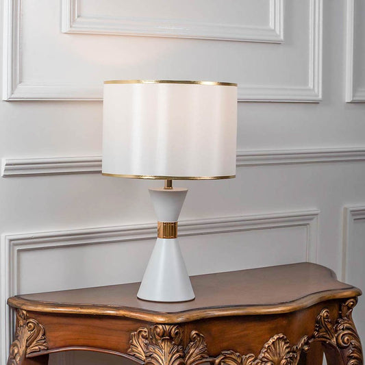 Table lamp with white ceramic base and wide fabric shade on wooden console table minimal classic lighting for home decor.