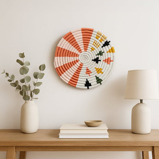 A multicolor woven wall plate styled above a wooden console with neutral decor accents creating a warm minimalist setting that highlights its textured handcrafted design.