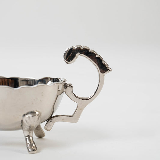 Detailed closeup view of the ornate scrolled handle and lion paw feet on the silver plated gravy boat on a white background.