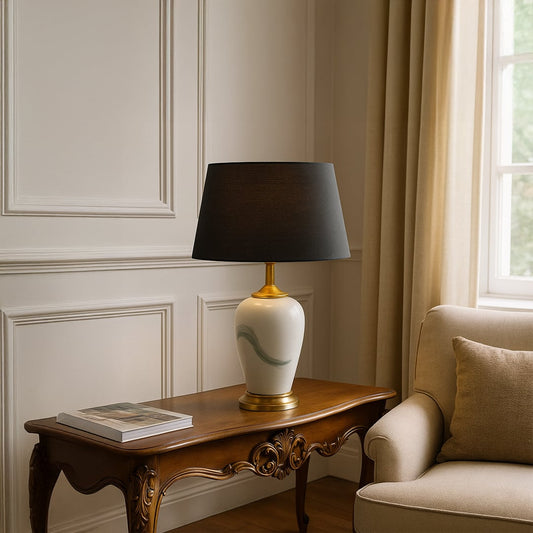 White ceramic table lamp with soft green brushstroke design gold base and black shade placed on a carved wooden side table adding a warm elegant touch to living room decor.