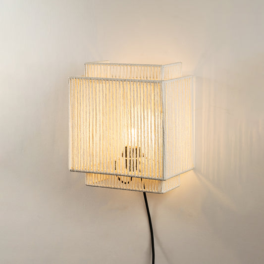 Wall light with pleated fabric shade emitting warm light ideal for bedroom or living room wall decor on clean white background.