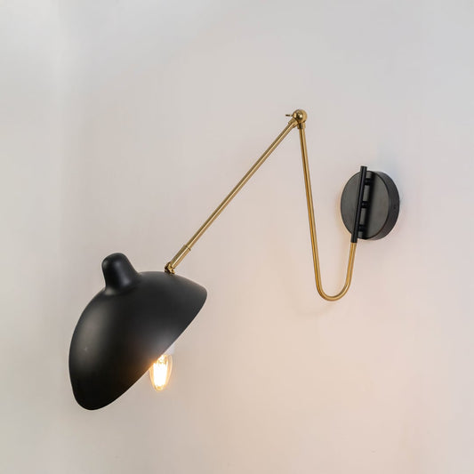 Wall lamp glowing with matte black shade adjustable gold arm and black base perfect for bedroom living room and study walls.