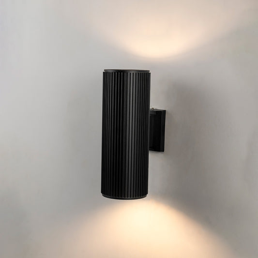 Black metal outdoor wall light glowing with upward downward beam lighting for modern exterior wall decor.
