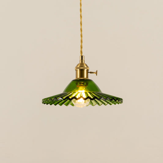 Illuminated green fluted metal pendant light with brass accents creating warm ambient lighting indoors.