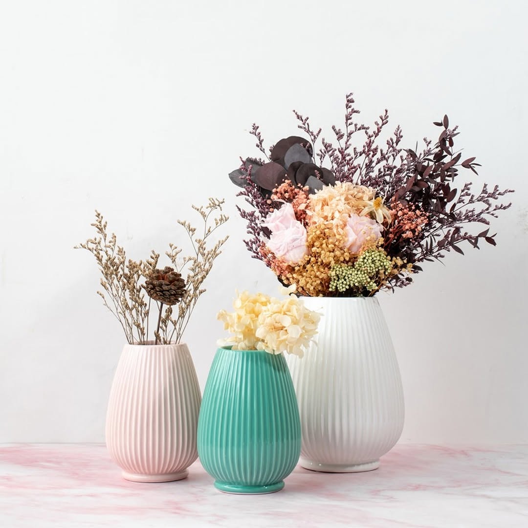 Pink ceramic vase displayed on a wooden coffee table in a cozy living room with mustard pillows and modern wall art.