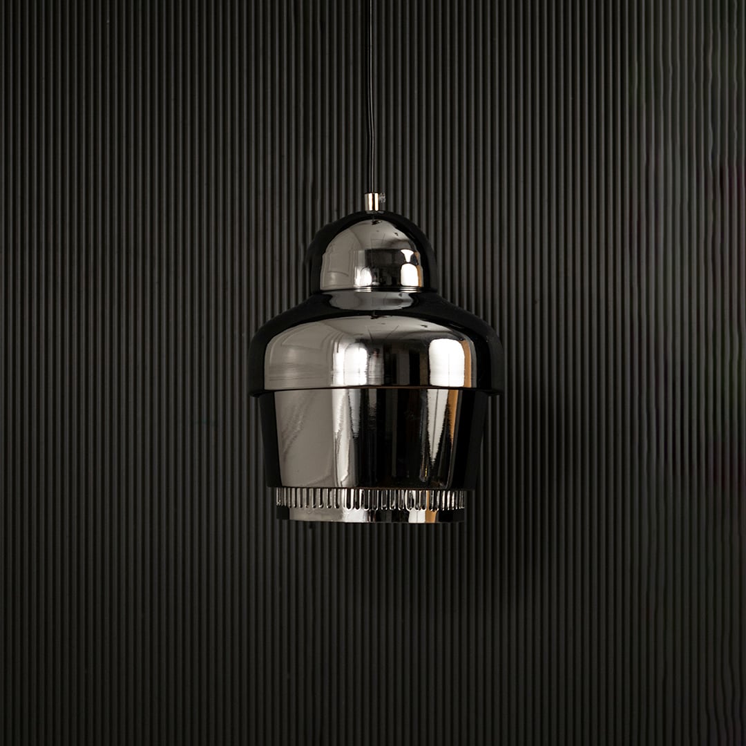 Chrome industrial pendant light with ribbed detailing hanging against dark textured wall with light off for sleek contemporary décor.