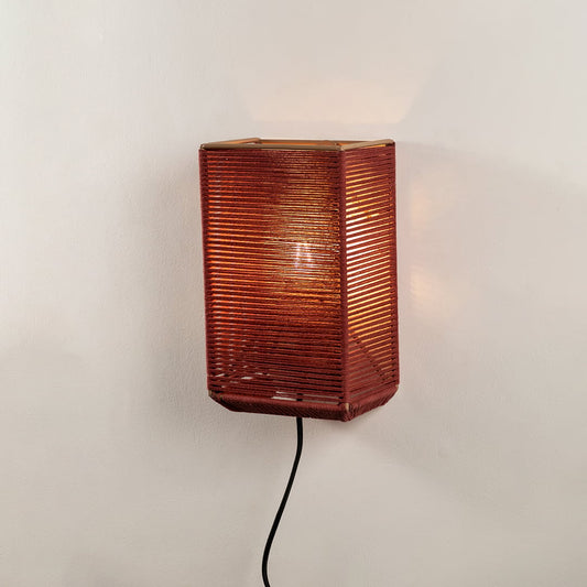 Modern rectangular rust red twine wall lamp turned on against a plain off white background to show the cozy light pattern.