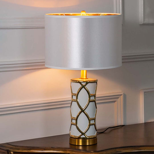 Gold metal table lamp with geometric lattice base and fabric drum shade creating refined luxury ambient lighting indoors.