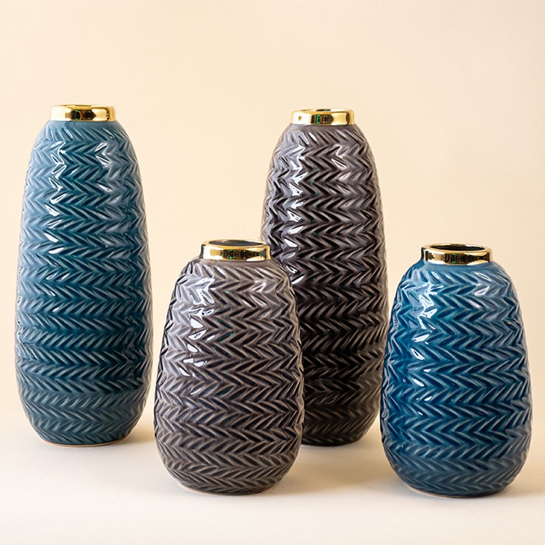 Collection of tall blue zigzag ceramic vases with gold detailing arranged together with pampas grass in a neutral interior setup.